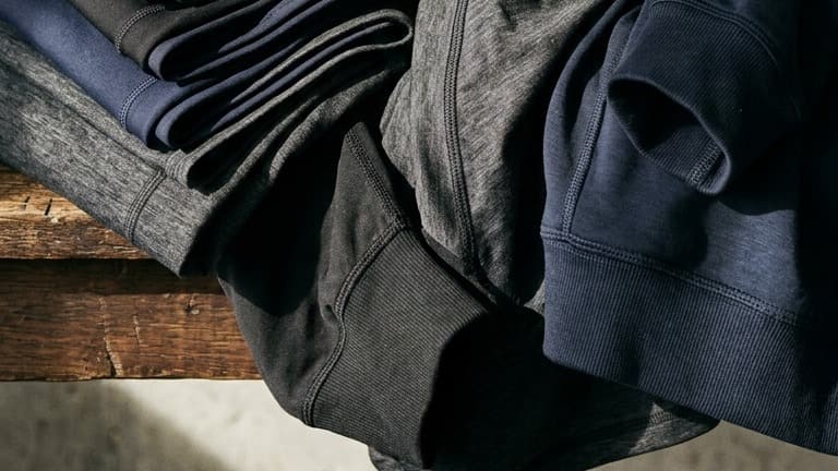 Folded dark gym clothes, marl and ribbed cuffs layered on a wooden bench