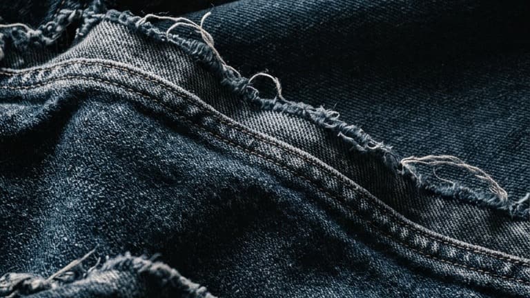 Layers of dark indigo denim with frayed hems crossing the frame as ridges