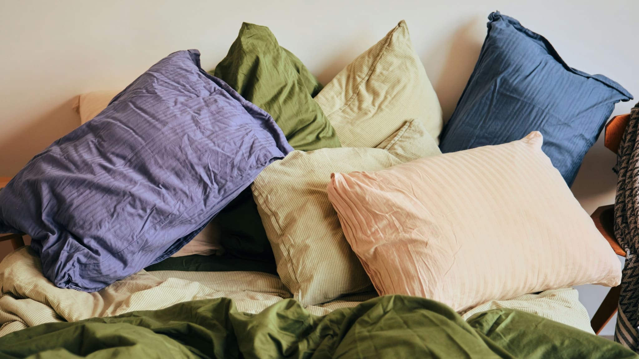 Pillows heaped against a headboard in purple, blue, green, cream and blush cases, an olive duvet rumpled in front