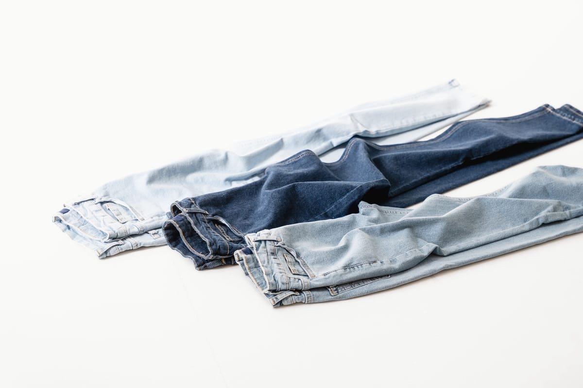 Three pairs of jeans laid out on pale ground, running from washed-pale to deep indigo